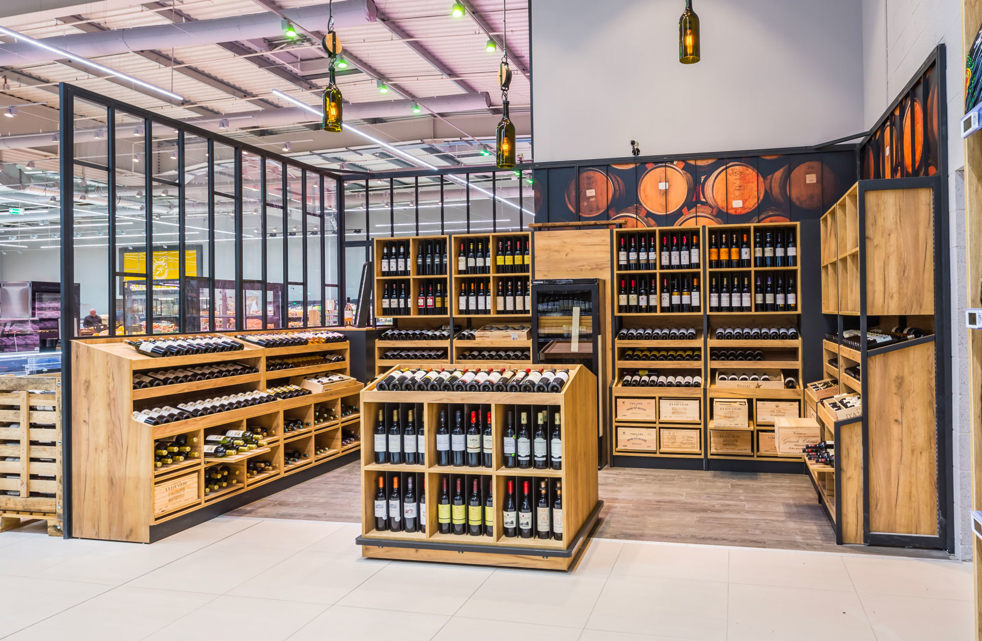 Section des vins dans un supermarché avec des bouteilles disposées sur des étagères et des caisses en bois d'une Réalisation Triangle Mobilier