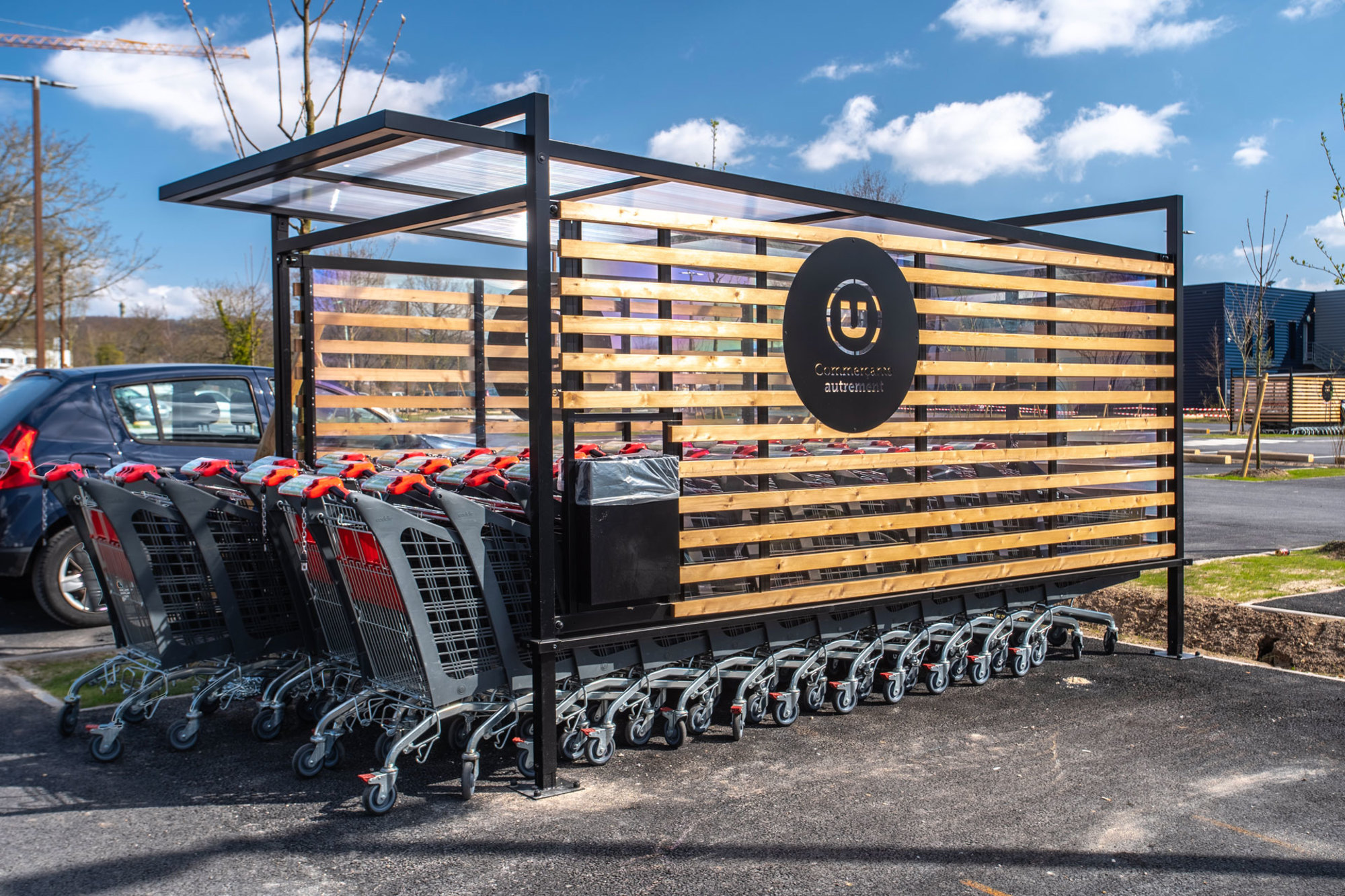 Station de chariots d'achat à l'extérieur d'un supermarché avec un design en bois et métal et un logo d'entreprise. Une réalisation Made In France par TriangleMobilier, concepteur fabricant de mobilier pour GMS.