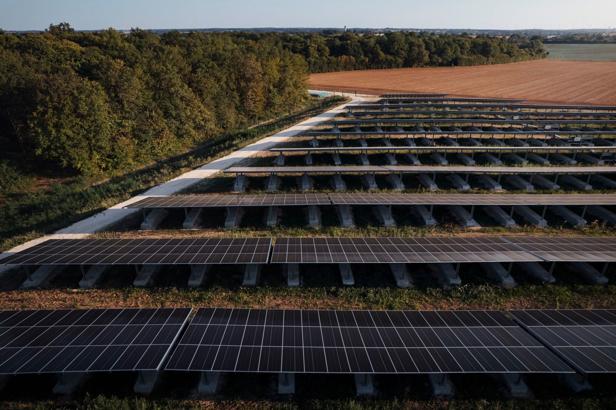 Une vue aérienne de panneaux solaires alignés dans un champ au coucher du soleil.